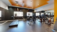 Located at 504 E Ninth St in Tucson, Arizona, this fitness center offers a comprehensive single-floor exercise facility designed to support a wide range of workout routines. The space is divided into distinct functional zones, making efficient use of its footprint for both cardio and strength training activities.

The cardio area features a row of treadmills and elliptical machines, each equipped with individual display screens for performance tracking. Full-length mirrors line one wall, visually expanding the space and allowing users to monitor their form. A textured dark accent wall, ceiling fan, and recessed lighting contribute to the room's energetic yet focused atmosphere, accented by a bold orange tray ceiling detail.

The strength training zone is anchored by a multi-station cable machine and a free weight rack stocked with a complete set of dumbbells, accompanied by an adjustable workout bench. Vibrant yellow accent walls display motivational text, reinforcing an encouraging workout environment. A water fountain is conveniently accessible nearby.

The functional training area includes an organized rack of stability balls, medicine balls, and resistance bands, alongside a treadmill and wall-mounted accessories. Durable rubber flooring throughout provides safety and comfort. Ceiling fans and recessed lighting ensure consistent airflow and visibility across the entire facility.