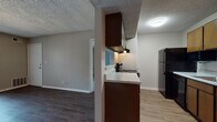 This single-floor unit is located at 7901 South Yale Avenue in Tulsa, Oklahoma, offering a practical and well-organized layout throughout. The kitchen is equipped with dark wood cabinetry, a light-toned countertop, a built-in range with overhead ventilation, a black refrigerator, and a dishwasher. Wood-look vinyl flooring runs through the kitchen and connects seamlessly to the adjacent living area. The living space is generously sized, featuring the same wood-look flooring, neutral taupe walls, and a large sliding glass door fitted with vertical blinds that allows an abundance of natural light to fill the room. The bedrooms are carpeted and offer comfortable dimensions, each with windows that bring in additional natural light. Two full bathrooms serve the unit, both featuring white tile tub-shower combinations, wood-look flooring, and clean, functional fixtures. One bathroom includes a double-sink vanity with dark wood cabinetry and a granite-style countertop, while the other conveniently houses a stacked washer and dryer unit. Throughout the space, a textured ceiling adds consistent character, and neutral tones create a cohesive, move-in-ready atmosphere.