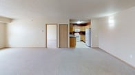 This single-floor residential unit offers a clean, functional layout designed for comfortable everyday living. The open-concept living area is finished with wall-to-wall carpet in a neutral tone, creating a warm and inviting atmosphere. The space flows directly into the kitchen, which is equipped with light oak cabinetry, dark laminate countertops, and white appliances including an electric range, over-the-range microwave, and refrigerator. A bold accent wall in deep red adds a touch of color to the kitchen area. A closet adjacent to the kitchen provides convenient additional storage. The bedroom is a generously sized, carpeted room brightened by two side-by-side windows fitted with blinds that offer views of the surrounding neighborhood. A wide reach-in closet with a rod and shelving provides ample storage. The full bathroom features tile flooring, an extended vanity with a large mirror, and a full-size tub and shower combination. Light wood trim and door accents are consistent throughout the unit, contributing to a cohesive and understated aesthetic. The textured ceilings and neutral wall tones throughout lend the space a clean, move-in-ready feel.