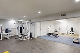 Located at 1281 Brockett Rd in Clarkston, GA, this fitness facility provides a generously sized, open-plan workout space across a single floor. The interior is finished with clean white walls and a combination of carpet, concrete, and area rug flooring, creating distinct functional zones throughout. Recessed ceiling lights and overhead fluorescent fixtures ensure bright, even illumination throughout the space.

The facility is equipped for a comprehensive workout experience. A multi-station cable machine and weight rack anchor one area, accompanied by an adjustable workout bench, a medicine ball rack, and exercise mats for floor work. A dedicated cardio zone features a treadmill and additional open floor space, marked with yellow safety striping. Stability balls, a lat pulldown machine, and a cable tower round out the strength training offerings.

Multiple entry and exit points are present, including a marked emergency exit door, contributing to safe accessibility. Windows along one wall allow for natural light and outdoor views of the surrounding greenery. HVAC vents are integrated into the ceiling, ensuring climate control throughout. The overall ambiance is clean, functional, and purposefully designed to support a variety of fitness activities in a well-maintained environment.