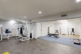 Located at 1281 Brockett Rd in Clarkston, GA, this fitness facility provides a generously sized, open-plan workout space across a single floor. The interior is finished with clean white walls and a combination of carpet, concrete, and area rug flooring, creating distinct functional zones throughout. Recessed ceiling lights and overhead fluorescent fixtures ensure bright, even illumination throughout the space.

The facility is equipped for a comprehensive workout experience. A multi-station cable machine and weight rack anchor one area, accompanied by an adjustable workout bench, a medicine ball rack, and exercise mats for floor work. A dedicated cardio zone features a treadmill and additional open floor space, marked with yellow safety striping. Stability balls, a lat pulldown machine, and a cable tower round out the strength training offerings.

Multiple entry and exit points are present, including a marked emergency exit door, contributing to safe accessibility. Windows along one wall allow for natural light and outdoor views of the surrounding greenery. HVAC vents are integrated into the ceiling, ensuring climate control throughout. The overall ambiance is clean, functional, and purposefully designed to support a variety of fitness activities in a well-maintained environment.