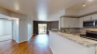 This single-story residence is designed with an open, flowing layout that connects the kitchen and living areas seamlessly. The kitchen features white cabinetry, granite countertops, a stone tile backsplash, stainless steel appliances, and a peninsula with a sink that overlooks the main living space. Wood-style flooring extends throughout the common areas, adding warmth and continuity.

The living room is anchored by a tile-surround fireplace and a sliding glass door that opens to an outdoor view, allowing natural light to fill the space. Contrasting gray accent walls add depth and a contemporary feel throughout.

The bedrooms are finished with plush carpet and offer generous walk-in closets with built-in shelving. The primary bedroom includes direct access to a private bathroom. The bathroom is well-appointed with a granite vanity, white cabinetry, and a tiled tub-shower combination featuring an elegant mosaic accent strip.

A dedicated laundry room accommodates a full-size washer and dryer, adding everyday convenience. Overall, the space presents a clean, modern aesthetic with functional, well-considered details throughout.
