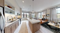 This single-floor residence showcases a thoughtfully designed open-concept layout that seamlessly connects the kitchen, dining, and living areas. The kitchen serves as the centerpiece, featuring a substantial island with a striking marble-look quartz countertop accommodating bar seating, complemented by two-tone cabinetry blending warm wood tones with crisp white upper cabinets. Stainless steel appliances, a subway tile backsplash, pendant lighting, and in-unit stacked laundry add both style and practicality. Black-framed windows throughout the unit flood the space with natural light and provide urban views, enhancing the modern aesthetic. The dining area accommodates a full-sized table beneath a cluster of globe pendant lights, while the living room offers a comfortable, eclectic atmosphere with built-in shelving. The bedroom is a serene retreat featuring generous closet space and large windows with urban views. Two bathrooms serve the unit: one features a walk-in tiled shower with a dark granite double vanity and marble-look tile flooring, while the second includes a tub-shower combination alongside built-in open shelving for added storage. Light wood-look flooring runs throughout the main living areas, unifying the space with a warm, contemporary feel.