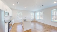 Located at 2950 Richmond Row Drive in Suwanee, Georgia, this single-floor residence offers a clean, modern design characterized by bright white walls, hardwood-style flooring, and an abundance of natural light. The open-concept kitchen and living area serves as the heart of the home, anchored by a central island with a granite countertop and undermount sink. White shaker cabinetry with sleek hardware lines the walls, complemented by a classic white subway tile backsplash and stainless steel appliances, including a range and over-the-range microwave. Multiple windows frame views of the surrounding wooded landscape, filling the space with natural light. A hallway connects the living areas to the private rooms, where plush carpeting and generously sized windows continue the theme of comfort and brightness. The bedrooms offer peaceful tree-lined views and ample wall space. The bathrooms are finished with granite-topped white vanities and hardwood-style flooring; one features a tub-shower combination with glass enclosure. Throughout the residence, recessed lighting, neutral tones, and consistent finishes create a cohesive, move-in-ready environment ideal for modern living.