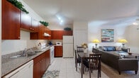 Located at 12400 Castlebridge Dr in Jersey Village, TX, this single-floor, 2-bedroom, 1-bathroom residence offers a practical and comfortable layout with well-defined living spaces. The kitchen is equipped with rich cherry wood cabinetry extending to the upper walls, a full suite of white appliances including a dishwasher, range, and refrigerator, and granite-style countertops with a double sink. Light-toned ceramic tile flooring runs throughout the kitchen and dining area, which flows naturally into the living room. The living room features plush carpet, crown molding, and a large window that admits natural light, creating a warm and inviting atmosphere. The primary bedroom is a comfortable retreat with carpet flooring, crown molding, a ceiling fan, and dual windows with blinds and sheer curtains that allow natural light while maintaining privacy. The second bedroom mirrors this restful aesthetic with its own window and wall-mounted television. The shared bathroom is finished with tile flooring, a cherry wood vanity with granite-style countertop, and a full tub-shower combination. A connecting hallway ties all rooms together efficiently. Overall, the space presents a cohesive, well-maintained interior with consistent warm-toned finishes throughout.