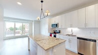 Located at 4021 Coon Rapids Blvd NW in Coon Rapids, Minnesota, this single-floor, 2-bedroom, 1-bathroom unit offers a thoughtfully designed layout that maximizes its comfortable footprint. The open-concept kitchen and living area serves as the heart of the home, featuring crisp white shaker cabinetry, a classic subway tile backsplash, granite countertops, and a central island that doubles as a prep and dining space. Stainless steel appliances — including a range, microwave, dishwasher, and refrigerator — complete the modern kitchen. Light hardwood flooring runs throughout the main living area, enhancing the bright, airy ambiance complemented by natural light from large windows. The two bedrooms are carpeted for comfort, with the primary bedroom offering a generous window with an outdoor view. The full bathroom includes a tub/shower combination, wood-style flooring, and a white vanity. Additional practical spaces include an in-unit laundry area and a utility room, adding everyday convenience. The overall design is clean and contemporary, with a neutral color palette that creates a welcoming and functional living environment.