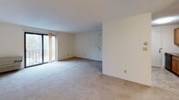 Located at 9 Village Hill Lane in Natick, Massachusetts, this single-floor unit offers a straightforward, functional layout across a comfortable footprint. The living area is generously sized, featuring neutral-toned wall-to-wall carpeting and soft, cream-colored walls that create a bright, understated ambiance. A sliding glass door provides direct access to a balcony, allowing natural light to filter into the space and offering views of surrounding greenery.

The galley-style kitchen runs parallel along two walls, outfitted with warm wood cabinetry, granite-look countertops, a stainless steel sink, and black appliances including a refrigerator and range. Light tile flooring completes the kitchen's practical design, and the layout allows for efficient use of the available space.

The bedroom is carpeted and features a window with natural tree views, providing a calm, private atmosphere. A sliding-door closet with built-in shelving offers organized storage. The full bathroom includes a tiled tub and shower surround with neutral stone-toned tiles, a vanity with a white countertop, wood cabinetry below, and tile flooring that ties the room together cohesively.