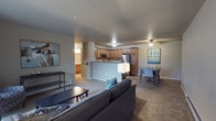 This single-floor residence offers a thoughtfully designed open-concept layout that seamlessly connects the living, dining, and kitchen areas. The living room features plush carpeting, large sliding glass doors that invite natural light, and ample space for comfortable seating arrangements. Adjacent to the living area, the kitchen is outfitted with warm wood cabinetry, granite-style countertops, a peninsula breakfast bar, and a full suite of stainless steel appliances including a refrigerator, range, microwave, and dishwasher. Light wood-style flooring runs throughout the kitchen and dining area, where a ceiling fan adds to the comfort of the space. The bedrooms are carpeted and generously sized, each featuring windows with blinds that allow for natural light. The primary bedroom includes a dresser with mirror and access to additional closet space, while a secondary room offers a dedicated closet and space suitable for a home office. The bathroom is well-appointed with a wood-toned vanity, granite-style countertop, a large mirror, and wood-style flooring. A standout feature is the spacious in-unit laundry room, complete with wire shelving and full-size washer and dryer hookups. Overall, the space presents a clean, functional, and inviting atmosphere throughout.