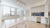 Located at 800 N 2nd St in Phoenix, AZ, this modern 2-bedroom, 2-bathroom residence offers a thoughtfully designed single-floor layout with contemporary finishes throughout. The open-concept kitchen serves as the heart of the home, showcasing white cabinetry with brushed nickel hardware, a striking navy blue herringbone tile backsplash, quartz countertops, and a full suite of stainless steel appliances. A generously sized curved kitchen island provides additional prep and dining space, illuminated by elegant geometric pendant lights that add a sculptural element to the space. Light wood-look flooring flows seamlessly throughout, enhancing the bright, airy atmosphere created by large windows with clean white walls. Both bedrooms are well-proportioned, bathed in natural light, and serviced by dedicated closet space with wire shelving. The primary bathroom features a dual-sink vanity with LED-backlit mirrors and ample cabinetry, while the second bathroom offers a soaking tub with marble-look tile surround and brushed gold fixtures. The overall design aesthetic is clean and modern, with a cohesive neutral palette accented by carefully chosen finishes that lend a polished, upscale feel throughout this Phoenix residence.