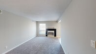 This single-floor unit offers a well-organized layout across several distinct living areas. The living room serves as the central gathering space, featuring plush gray carpeting, neutral gray walls, a textured ceiling, and a fireplace with a contrasting black surround and white mantel. A window provides natural light, while a sliding glass door fitted with vertical blinds opens to an outdoor view of a landscaped communal area.

The galley-style kitchen is efficiently designed with warm oak cabinetry lining both sides, granite-look countertops, a double stainless steel sink, and white appliances including an electric range and refrigerator. Light ceramic tile flooring runs throughout, and a dedicated pantry closet adds practical storage. The kitchen connects openly to a dining or transitional area, creating a functional flow.

The bedrooms are carpeted and finished in soft neutral tones, each offering natural light through windows and ample wall space. Closet access is available within the bedroom areas. The bathroom features a full tub-shower combination with clean white square tile surround. Throughout the unit, white baseboards and consistent neutral paint create a cohesive, understated aesthetic suited for a range of furnishing styles.