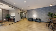 Located at 750 Summer St in Stamford, Connecticut, this thoughtfully designed commercial space delivers a polished and professional atmosphere across two distinct areas. Light hardwood flooring flows seamlessly throughout, anchoring a cohesive and contemporary aesthetic.

The reception and lounge area makes a strong first impression with a bold geometric-patterned feature wall in cool blue-grey tones. Sleek black leather seating paired with a marble accent table and elegant floor lamps create a refined waiting environment. A glass-partitioned corridor leads to a private office or consultation room, visible through floor-to-ceiling glass panels that enhance openness and transparency while maintaining separation.

The adjoining communal area is bright and inviting, benefiting from large floor-to-ceiling windows that draw in generous natural light and offer views to the outdoors. A long communal table with industrial-style stools serves as a central gathering point, complemented by lush greenery and curated wall art. A dedicated meeting nook features a striking round black marble table, warm wood-and-gold chairs, a wall-mounted display screen, and the same signature geometric wallcovering, making it ideal for focused discussions or presentations. Recessed and pendant lighting throughout ensures a well-lit, welcoming environment suited for a variety of professional uses.