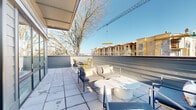 Located at 720 E 36th St in Charlotte, NC, this single-level outdoor terrace offers a generous open-air living experience in the heart of a dynamic urban neighborhood. The terrace is designed with a clean, modern aesthetic, featuring large-format tile pavers that extend across the full expanse of the space, providing a polished and durable surface underfoot.

The terrace is divided into two functional zones. A lounge area is furnished with contemporary seating, including a sleek sofa, accent chairs, and a round pedestal coffee table, creating a comfortable setting for relaxation or casual gatherings. Adjacent to this, a dedicated dining area accommodates a rectangular table paired with woven rattan chairs, ideal for outdoor meals.

The space benefits from abundant natural light throughout the day, with an open sky above and partial overhead coverage along one edge providing shade. Low perimeter railings and panel barriers frame the terrace while preserving broad sightlines. Views extend outward to mature trees, the surrounding Charlotte neighborhood rooftops, and glimpses of the city skyline in the distance. The elevated position of the terrace further enhances the sense of openness and connectivity to the surrounding urban environment.