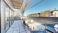 Located at 720 E 36th St in Charlotte, NC, this single-level outdoor terrace offers a generous open-air living experience in the heart of a dynamic urban neighborhood. The terrace is designed with a clean, modern aesthetic, featuring large-format tile pavers that extend across the full expanse of the space, providing a polished and durable surface underfoot.

The terrace is divided into two functional zones. A lounge area is furnished with contemporary seating, including a sleek sofa, accent chairs, and a round pedestal coffee table, creating a comfortable setting for relaxation or casual gatherings. Adjacent to this, a dedicated dining area accommodates a rectangular table paired with woven rattan chairs, ideal for outdoor meals.

The space benefits from abundant natural light throughout the day, with an open sky above and partial overhead coverage along one edge providing shade. Low perimeter railings and panel barriers frame the terrace while preserving broad sightlines. Views extend outward to mature trees, the surrounding Charlotte neighborhood rooftops, and glimpses of the city skyline in the distance. The elevated position of the terrace further enhances the sense of openness and connectivity to the surrounding urban environment.