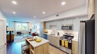 Located at Mainplace Dr in Santa Ana, CA, this well-designed two-bedroom, two-bathroom apartment offers a thoughtful single-floor layout ideal for comfortable living. The open-concept kitchen and living area serves as the heart of the home, featuring a central island with a white quartz countertop and bar seating, warm wood-tone cabinetry paired with soft sage upper cabinets, and a classic white subway tile backsplash. Stainless steel appliances, including a gas range, microwave, dishwasher, and refrigerator, complete the modern culinary space. The living room receives generous natural light through large windows with outdoor views, and durable wood-style flooring runs throughout the main living areas. The primary bedroom is a comfortable retreat, highlighted by a bold accent wall, plush carpeting, and a spacious walk-in closet with built-in shelving. The second bedroom offers a similar level of comfort and natural light. Both bathrooms are finished with clean, modern tile work, including a tiled tub-shower combination and wood-style flooring. A dedicated hallway connects the rooms efficiently, contributing to the home's well-organized flow. Recessed lighting throughout adds to the bright, contemporary ambiance of this Santa Ana residence.