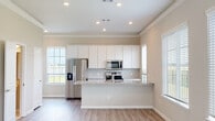 This two-story home is designed with a clean, contemporary aesthetic and a neutral color palette that creates a bright, welcoming atmosphere throughout. The main living level centers around an open-concept kitchen and living area, where light hardwood-style flooring and crown molding add a polished finish. The kitchen is a standout feature, equipped with crisp white cabinetry extending to the ceiling, a subway tile backsplash, and granite countertops that carry across both the large central island and the perimeter surfaces. Stainless steel appliances, including a French door refrigerator, built-in microwave, and range, complete the functional layout. Recessed lighting and multiple windows allow natural light to fill the space, offering outdoor views and keeping the interior open and airy.

The adjacent living area is generously proportioned, with a bank of windows that further enhance the sense of light and space. Upstairs, the bedrooms feature plush carpeting, ceiling fans, and natural light from well-placed windows. A secondary bedroom is accessed through an elegant arched entryway with a vaulted ceiling. Bathrooms are finished with granite vanity tops, white cabinetry, and tile surrounds, maintaining a consistent level of quality and detail throughout the home.