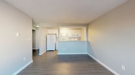 Located at 2136 West Riverside Avenue in Spokane, Washington, this well-appointed single-floor unit offers a clean, modern aesthetic throughout. The space features durable dark wood-look luxury vinyl plank flooring that runs consistently across all rooms, complemented by crisp white baseboards and neutral gray walls that create a fresh, contemporary feel. Textured ceilings add a classic touch overhead.

The open living area is generously sized and filled with natural light from large windows that frame views of surrounding trees and the neighborhood beyond. Baseboard heating units are positioned beneath the windows in both the living and bedroom areas, ensuring comfortable warmth throughout. The layout flows seamlessly into the kitchen, which is accessible via a convenient pass-through opening with a light granite-style countertop. The kitchen is equipped with white shaker-style cabinetry, a double basin sink, a full-size top-freezer refrigerator, a microwave, and ample counter and storage space.

The bedroom offers a well-proportioned, quiet retreat with the same cohesive flooring and neutral tones found throughout. The bathroom features a full tub and shower combination, accented by white and soft blue tile detailing that adds a subtle decorative element. Overall, the space presents a clean, move-in-ready interior with a cohesive design palette in a convenient Spokane location.