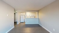 Located at 2136 West Riverside Avenue in Spokane, Washington, this well-appointed single-floor unit offers a clean, modern aesthetic throughout. The space features durable dark wood-look luxury vinyl plank flooring that runs consistently across all rooms, complemented by crisp white baseboards and neutral gray walls that create a fresh, contemporary feel. Textured ceilings add a classic touch overhead.

The open living area is generously sized and filled with natural light from large windows that frame views of surrounding trees and the neighborhood beyond. Baseboard heating units are positioned beneath the windows in both the living and bedroom areas, ensuring comfortable warmth throughout. The layout flows seamlessly into the kitchen, which is accessible via a convenient pass-through opening with a light granite-style countertop. The kitchen is equipped with white shaker-style cabinetry, a double basin sink, a full-size top-freezer refrigerator, a microwave, and ample counter and storage space.

The bedroom offers a well-proportioned, quiet retreat with the same cohesive flooring and neutral tones found throughout. The bathroom features a full tub and shower combination, accented by white and soft blue tile detailing that adds a subtle decorative element. Overall, the space presents a clean, move-in-ready interior with a cohesive design palette in a convenient Spokane location.