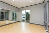 Located at 1345 Hardeman Ave in Macon, Georgia, this single-floor fitness facility offers a well-appointed layout designed to support a variety of exercise and wellness activities. The space is divided into two primary areas: a dedicated fitness room and an adjoining studio room, connected by a glass-paneled door that maintains visual openness between the two zones.

The fitness room is equipped with cardio machines, including treadmills, and additional strength and conditioning equipment. A ceiling fan provides climate comfort, and the room benefits from large windows that invite natural light while offering views of the surrounding greenery.

The studio room is a bright, open space finished with smooth light wood flooring that runs throughout both areas. Floor-to-ceiling mirrors line the walls of the studio, creating an expansive feel and making the room ideal for yoga, dance, stretching, or group fitness classes. Large windows along one wall frame views of mature trees and landscaping, enhancing the room's connection to the outdoors.

Throughout the facility, the design is clean and modern, characterized by gray-toned walls, dark crown molding, and recessed lighting. The overall ambiance is functional yet polished, providing a professional environment suited for a range of fitness and wellness uses.