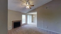 This single-floor home offers an open-concept layout that connects the living and dining areas seamlessly. The living room is a welcoming focal point, featuring vaulted ceilings with a ceiling fan and light fixture that enhance the sense of spaciousness. A brick-surround fireplace with a black insert serves as a standout architectural element along one wall, adding character and a cozy ambiance to the room. Natural light enters through a window and sliding glass door dressed with vertical blinds, brightening the neutral-toned, carpeted floors throughout.

A wide open passage leads from the living room into the adjoining dining area, which is distinguished by its own pendant light fixture hanging overhead — a subtle yet functional design detail. The textured ceiling treatment is consistent throughout both spaces, contributing to a cohesive aesthetic. Neutral wall tones complement the warm carpeting, creating a versatile backdrop well-suited to a variety of furnishing styles. The overall layout promotes an easy flow between living and dining spaces, making the home feel connected and functional.