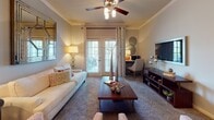 This thoughtfully designed single-floor residence offers a cohesive and comfortable living environment across several well-defined spaces. The living room serves as the heart of the home, featuring elegant crown molding, a ceiling fan with integrated lighting, and French doors that invite natural light and provide outdoor access. A large decorative mirror and warm ambient lighting contribute to the room's inviting atmosphere.

The dedicated dining area is finished with carpet flooring, crown molding, and a modern chandelier overhead, creating an ideal setting for shared meals. Adjacent to it, the kitchen is outfitted with dark cabinetry, black appliances, a tile backsplash, and rich hardwood-style flooring, offering a striking contrast and ample storage.

The residence includes multiple bedrooms, each carpeted and equipped with ceiling fans. The bedrooms feature large windows dressed with layered curtains that allow for natural light and outdoor views, along with generous space for furnishings. The bathrooms are well-appointed with dark vanity cabinetry, light countertops, tile flooring, and a full tub-shower combination. Throughout the home, a consistent neutral color palette and warm accent tones create a unified and welcoming ambiance.