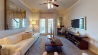 This thoughtfully designed single-floor residence offers a cohesive and comfortable living environment across several well-defined spaces. The living room serves as the heart of the home, featuring elegant crown molding, a ceiling fan with integrated lighting, and French doors that invite natural light and provide outdoor access. A large decorative mirror and warm ambient lighting contribute to the room's inviting atmosphere.

The dedicated dining area is finished with carpet flooring, crown molding, and a modern chandelier overhead, creating an ideal setting for shared meals. Adjacent to it, the kitchen is outfitted with dark cabinetry, black appliances, a tile backsplash, and rich hardwood-style flooring, offering a striking contrast and ample storage.

The residence includes multiple bedrooms, each carpeted and equipped with ceiling fans. The bedrooms feature large windows dressed with layered curtains that allow for natural light and outdoor views, along with generous space for furnishings. The bathrooms are well-appointed with dark vanity cabinetry, light countertops, tile flooring, and a full tub-shower combination. Throughout the home, a consistent neutral color palette and warm accent tones create a unified and welcoming ambiance.