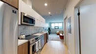 Located on the iconic Wilshire Boulevard in the heart of Los Angeles, this modern studio offers a thoughtfully designed open-concept layout that maximizes every inch of space. Light-toned hardwood flooring flows throughout, creating a warm and cohesive feel across all areas.

The galley-style kitchen is well-appointed with stainless steel appliances, including a full-size refrigerator, electric range, over-the-range microwave, and dishwasher. White upper cabinetry is paired with warm wood lower cabinets, and a marble-style tile backsplash adds a refined touch. Ample counter space makes the kitchen as functional as it is attractive.

The open living area is bright and inviting, featuring a large window that brings in natural light and city views. The space comfortably accommodates a full seating arrangement alongside a sleeping area, demonstrating the versatility of the floor plan. Recessed lighting throughout keeps the ambiance clean and modern.

The bathroom is finished with a wood-toned vanity, white quartz countertop, a large mirror, and a tiled shower-tub combination, maintaining the contemporary aesthetic carried throughout the unit. Overall, this space presents a sleek, efficiently planned urban residence with modern finishes and a comfortable, livable design.