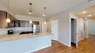 This single-floor unit offers a thoughtfully designed open layout that seamlessly connects the living and kitchen areas. The kitchen is a standout feature, boasting rich dark cabinetry, light granite countertops, a classic white subway tile backsplash, and a full suite of stainless steel appliances including a range, microwave, and refrigerator. A peninsula with pendant lighting serves as both a functional workspace and an inviting gathering point. Warm hardwood-style flooring runs throughout the entire unit, creating a cohesive and inviting atmosphere. The living area is generously sized and benefits from large windows that usher in abundant natural light, with views of the surrounding neighborhood and a convenient exterior door providing direct outdoor access. The bedroom is a comfortable retreat, complete with a ceiling fan and a walk-in closet offering ample storage. A second well-lit room with multiple windows provides flexibility as a bedroom, office, or den. The bathroom is clean and functional, featuring a granite-topped vanity with dark cabinetry, a full tub-shower combination, and consistent hardwood-style flooring. Neutral gray walls throughout lend a modern, move-in-ready feel to the entire space.