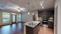 This well-appointed single-floor residence offers a thoughtfully designed open-concept layout that seamlessly connects the kitchen and living areas. The kitchen is a standout feature, showcasing dark espresso cabinetry, granite countertops, a tile backsplash, and a full suite of stainless steel appliances including a refrigerator, range, microwave, and dishwasher. A central island with an integrated sink and pendant lighting above adds both style and functionality, while track lighting illuminates the workspace effectively.

The living area is defined by rich hardwood-style flooring, a tray ceiling with crown molding, and a ceiling fan, contributing to a polished and comfortable ambiance. Natural light filters in through windows fitted with blinds, and a door provides access to an outdoor area.

The bedrooms feature soft carpeting, generous windows, and ceiling fans, offering a quiet and comfortable retreat. Two full bathrooms maintain the design consistency of the unit, each featuring dark wood vanities with granite countertops and large mirrors. One bathroom includes a combination tub and shower, while the other presents a spacious vanity with ample cabinet storage and bright overhead lighting. Neutral tones throughout create a clean, cohesive aesthetic.