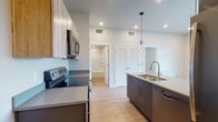 This well-appointed single-floor unit showcases a clean, contemporary design throughout. The open-concept kitchen serves as the centerpiece, featuring dark cabinetry with sleek hardware, a bold teal island with a double-basin sink and pendant lighting overhead, and a full suite of stainless steel appliances including an electric range, over-the-range microwave, refrigerator, and dishwasher. Light wood-toned upper cabinets and a subtle tile backsplash add visual contrast and warmth to the space. Light hardwood-style flooring flows seamlessly throughout the entire unit, enhancing the sense of openness and continuity. The bedroom is a bright, comfortable retreat, benefiting from a large window that frames an urban cityscape, flooding the room with natural light. A louvered closet provides convenient built-in storage. The bathroom is finished with consistent, modern detailing — dark cabinetry with a quartz-style countertop, a full tub and shower combination with tiled surround and built-in shelving, recessed lighting, and hardwood-style flooring. In-unit laundry is also present, adding everyday practicality. The overall ambiance is modern, fresh, and functional, with a cohesive color palette and quality finishes throughout.
