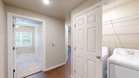 This single-story residence located in Rogers, Arkansas, presents a thoughtfully designed interior finished with a neutral, warm color palette throughout. The layout connects living areas seamlessly, with durable wood-style flooring extending through the main living spaces, hallways, and kitchen, while plush carpet adds comfort to the bedrooms.

The living area is an open, well-proportioned space featuring a ceiling fan with integrated lighting and a window fitted with blinds that allows natural light to filter in. Adjacent to the living area, the kitchen is equipped with dark-toned cabinetry, granite-style countertops, and a full suite of stainless steel appliances including a refrigerator, electric range, built-in microwave, and dishwasher. A window above the kitchen area provides additional natural light and outdoor views.

The bedrooms are comfortably sized, each featuring ceiling fans and windows with blinds, some of which offer views of surrounding greenery. The bathrooms are consistently finished with dark wood vanity cabinetry, white countertops, round mirrors, and tub-shower combinations enclosed by sliding glass doors. Additional storage is provided by wall-mounted cabinetry in the bathrooms. A dedicated laundry area with wire shelving is accessible via the main hallway, complementing the overall functional design of the space.