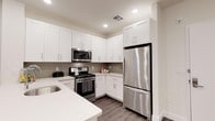This well-appointed single-floor residence offers a clean, contemporary aesthetic defined by thoughtful design and quality finishes. The kitchen serves as a standout feature, showcasing crisp white shaker-style cabinetry that extends to the ceiling for ample storage, paired with light quartz countertops that lend a bright, open feel to the space. A tasteful gray tile backsplash adds subtle texture and contrast, complementing the stainless steel appliance suite that includes a gas range, over-the-range microwave, and a full-size refrigerator. Recessed lighting illuminates the kitchen evenly, highlighting the clean lines and modern hardware throughout. The dark hardwood-style flooring grounds the space with warmth and durability, creating a striking contrast against the light cabinetry and walls. The neutral color palette of soft whites and warm grays flows cohesively through the space, creating a calm and inviting ambiance. The overall layout is efficient and functional, making excellent use of the available footprint while maintaining an uncluttered, modern look. This space is ideal for those who appreciate contemporary design paired with practical, everyday livability.