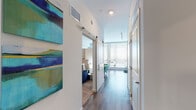 Located in the heart of Orlando, Florida, this single-floor residence at 355 N Rosalind Ave offers a thoughtfully designed open-concept layout that blends contemporary style with everyday functionality. The space is unified by warm wood-tone flooring that flows seamlessly throughout, creating a cohesive and inviting atmosphere.

The kitchen is a standout feature, outfitted with dark, floor-to-ceiling cabinetry, light quartz countertops, a tile backsplash, and a full suite of stainless steel appliances including a refrigerator, electric range, over-the-range microwave, and dishwasher. The kitchen opens directly to the living area, which benefits from natural light through large windows fitted with horizontal blinds. The living space accommodates a comfortable seating arrangement, an entertainment center, and a dedicated workspace with a desk — ideal for both relaxation and productivity.

A hallway with sliding barn doors leads to the bedroom, which features carpeted flooring for added comfort. Colorful wall art accents the corridor, adding a vibrant, modern touch to the transition spaces. The bathroom is clean and contemporary, featuring dark vanity cabinetry, a white countertop sink, a well-lit mirror, and a walk-in shower with glass enclosure. The overall ambiance of this residence is modern, bright, and efficiently designed for comfortable urban living.