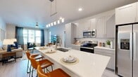 Located at 8925 77th Terrace East in the sought-after community of Lakewood Ranch, Florida, this single-floor residence offers a thoughtfully designed open-concept layout finished with light wood-style flooring and a neutral palette throughout. The kitchen is a standout feature, boasting an expansive quartz waterfall island with bar seating, gray shaker-style cabinetry, a classic subway tile backsplash, stainless steel appliances, and contemporary pendant lighting — all flowing seamlessly into the bright and airy living area. The living room is well-lit by large windows with views to the outdoors, creating an inviting atmosphere ideal for relaxing or entertaining. Two well-appointed bedrooms each feature ceiling fans and windows that bring in natural light. The primary bedroom connects to a generously sized walk-in closet with built-in wire shelving. The bathroom presents a clean, modern aesthetic with a quartz-topped vanity, light cabinetry, and a glass-enclosed shower. A dedicated in-unit laundry room with full-size washer and dryer adds everyday convenience. The overall ambiance is bright, contemporary, and move-in ready, reflecting the relaxed yet refined lifestyle characteristic of Lakewood Ranch.