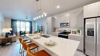 Located at 8925 77th Terrace East in the sought-after community of Lakewood Ranch, Florida, this single-floor residence offers a thoughtfully designed open-concept layout finished with light wood-style flooring and a neutral palette throughout. The kitchen is a standout feature, boasting an expansive quartz waterfall island with bar seating, gray shaker-style cabinetry, a classic subway tile backsplash, stainless steel appliances, and contemporary pendant lighting — all flowing seamlessly into the bright and airy living area. The living room is well-lit by large windows with views to the outdoors, creating an inviting atmosphere ideal for relaxing or entertaining. Two well-appointed bedrooms each feature ceiling fans and windows that bring in natural light. The primary bedroom connects to a generously sized walk-in closet with built-in wire shelving. The bathroom presents a clean, modern aesthetic with a quartz-topped vanity, light cabinetry, and a glass-enclosed shower. A dedicated in-unit laundry room with full-size washer and dryer adds everyday convenience. The overall ambiance is bright, contemporary, and move-in ready, reflecting the relaxed yet refined lifestyle characteristic of Lakewood Ranch.