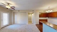 Located at 6885 W Lone Mountain Rd in Las Vegas, Nevada, this one-bedroom, one-bathroom residence offers a well-designed, single-floor layout that makes efficient use of its space. The open-concept living and kitchen area forms the heart of the unit, where rich wood-tone cabinetry, granite countertops, and stainless steel appliances — including a gas range, microwave, and refrigerator — create a functional and attractive kitchen. Wood-style flooring runs throughout the kitchen and dining area, while a chandelier and track lighting add a warm, layered glow. The living room features plush carpeting, a ceiling fan with light fixture, and a built-in desk nook, along with a private entry door and windows that allow natural light to filter in. A hallway with an arched accent connects the main living area to the private bedroom, which is carpeted, ceiling fan-equipped, and includes a closet with built-in shelving. The bathroom is appointed with a full soaking tub and shower combination featuring tiled surround and built-in shelving niches. Central HVAC vents are present throughout, ensuring year-round comfort in the Las Vegas climate.
