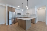 Located at 155 Greenbrier Rd in Cambridge, Ontario, this well-appointed 2-bedroom, 2-bathroom unit offers a thoughtfully designed single-level layout with a clean, contemporary aesthetic throughout. Light-toned hardwood flooring flows seamlessly across the living spaces, complementing the bright white walls and modern finishes.

The open-concept kitchen and living area forms the heart of the unit. The kitchen is equipped with stainless steel appliances — including a full-size refrigerator, stove, built-in microwave, and dishwasher — alongside two-tone cabinetry featuring white upper cabinets and warm wood-grain lower cabinets. A central island with a white quartz countertop and pendant lighting above provides additional prep space and casual seating. The adjacent living room is filled with natural light from a large picture window that offers outdoor views.

The spacious primary bedroom includes its own walk-in closet fitted with wire shelving rods. The second bedroom also benefits from a closet. Both bathrooms are finished with neutral tile work, warm wood vanities, and white quartz countertops — one featuring a sleek sliding glass shower enclosure and the other a full soaker tub. The overall ambiance is fresh, modern, and move-in ready.