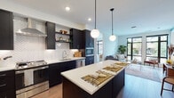 Located at 401 Wythe Street in Alexandria, Virginia, this single-floor residence offers a thoughtfully designed layout with contemporary finishes throughout. The open-concept kitchen serves as a central focal point, showcasing dark shaker cabinetry, a striking white herringbone-pattern tile backsplash, stainless steel appliances including a gas range and French door refrigerator, and a generously sized island with a white quartz countertop illuminated by globe pendant lights. Light hardwood flooring extends seamlessly into the adjacent living area, where oversized black-framed windows flood the space with natural light and offer views of the surrounding Alexandria streetscape.

The bedrooms are well-proportioned and bright, each benefiting from large windows with street-facing views. The primary bedroom connects directly to a walk-in closet and an en-suite bathroom featuring a glass-enclosed subway tile shower and a classic black-and-white mosaic tile floor. A second full bathroom echoes this aesthetic with a coordinating vanity, tiled shower, and the same distinctive dotted floor tile. An in-unit stacked washer and dryer adds everyday convenience. The overall design balances modern sophistication with warm, livable touches throughout.