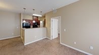 Located at 1000 Parker Cone Way in Greenville, SC, this single-floor residence offers a thoughtfully designed open-concept layout finished in warm, neutral tones throughout. The living area is generously proportioned, featuring plush wall-to-wall carpeting, a ceiling fan, and a seamless connection to the kitchen via a peninsula-style breakfast bar. Pendant lighting illuminates the kitchen, which is appointed with rich dark wood cabinetry, granite-style countertops, tile flooring, and black appliances including a refrigerator, electric range with overhead microwave, and ample upper and lower cabinet storage. The bedrooms are well-sized, each featuring soft carpeting, double windows dressed with blinds that invite natural light, and ceiling-mounted light fixtures. The bathrooms are finished with tile flooring, warm-toned walls, and include a full tub-and-shower combination with a chrome curtain rod. One bathroom features a dark wood vanity with a single sink and a lighted mirror above, accompanied by a spacious walk-in closet with built-in wire shelving. Clean white panel doors, white trim, and consistent warm beige walls create a cohesive, welcoming ambiance throughout the entire space.
