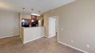 Located at 1000 Parker Cone Way in Greenville, SC, this single-floor residence offers a thoughtfully designed open-concept layout finished in warm, neutral tones throughout. The living area is generously proportioned, featuring plush wall-to-wall carpeting, a ceiling fan, and a seamless connection to the kitchen via a peninsula-style breakfast bar. Pendant lighting illuminates the kitchen, which is appointed with rich dark wood cabinetry, granite-style countertops, tile flooring, and black appliances including a refrigerator, electric range with overhead microwave, and ample upper and lower cabinet storage. The bedrooms are well-sized, each featuring soft carpeting, double windows dressed with blinds that invite natural light, and ceiling-mounted light fixtures. The bathrooms are finished with tile flooring, warm-toned walls, and include a full tub-and-shower combination with a chrome curtain rod. One bathroom features a dark wood vanity with a single sink and a lighted mirror above, accompanied by a spacious walk-in closet with built-in wire shelving. Clean white panel doors, white trim, and consistent warm beige walls create a cohesive, welcoming ambiance throughout the entire space.
