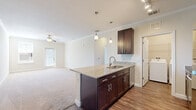This well-appointed one-bedroom, one-bathroom unit in Orlando, FL offers a thoughtfully designed open-concept layout. The combined kitchen and living area serves as the heart of the home, where dark espresso cabinetry, granite countertops, and a kitchen island with a built-in sink create a functional and stylish cooking space. Stainless steel appliances, track lighting, and elegant pendant lights above the island complete the kitchen. Crown molding accents the living area, which features plush carpet flooring, a ceiling fan, and access to a private balcony with natural light streaming through the glass door and adjacent window. Wood-style flooring runs through the kitchen and wet areas, while soft carpet covers the living and bedroom spaces. The generously sized bedroom includes a large window for natural light and direct access to a spacious walk-in closet outfitted with wire shelving systems for ample storage. The bathroom is finished with a dark wood vanity topped with granite, wood-style flooring, and a tub-shower combination adorned with large-format marble-look tile and a decorative mosaic accent border. A dedicated laundry area with full-size washer and dryer hookups adds everyday convenience to this efficiently designed home.