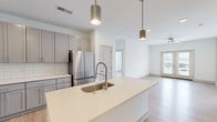 Located at Muse Carmel in Carmel, Indiana, this thoughtfully designed 3-bedroom, 2-bathroom residence offers a bright, modern living experience on a single floor. The open-concept kitchen and living area serves as the heart of the home, featuring gray shaker cabinetry, a white subway tile backsplash, stainless steel appliances including a range, microwave, and refrigerator, and a large center island with quartz countertops and an undermount sink. Sleek cylindrical pendant lights and light wood-style flooring complete the contemporary aesthetic. The living area extends to a set of French doors that open to a balcony, filling the space with natural light and outdoor views. The bedrooms are carpeted for comfort and outfitted with ceiling fans and windows that allow ample natural light. The spacious primary bedroom includes a generously sized walk-in closet with wire shelving, while a second walk-in closet provides additional storage. The bathrooms are finished with quartz vanities, gray cabinetry, and wood-look tile flooring. The primary bath features a glass-enclosed walk-in shower with white subway tile. A dedicated laundry room houses a full-size washer and dryer with overhead wire shelving, adding everyday convenience to this well-appointed residence.