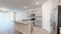 Located at 6568 Halo Bend Court in Wesley Chapel, FL, this well-appointed two-story home offers a thoughtful layout spread across two floors. The main level features an open-concept kitchen and living area bathed in natural light from large sliding glass doors, complete with a ceiling fan and light wood-style flooring that flows throughout. The kitchen is a standout, showcasing gray shaker-style cabinetry, granite countertops, a center island with a sink, and a full suite of stainless steel appliances including a refrigerator, range, and built-in microwave. A convenient half bathroom on the main floor is finished with matching granite counters and gray cabinetry. An attached garage with an automatic opener provides direct interior access. Upstairs, the open landing with a decorative railing leads to three well-sized bedrooms, each featuring light wood-style flooring and windows that invite natural light. The spacious primary bedroom includes its own closet and ensuite access. Four closets throughout the home provide ample storage. With a clean, neutral palette, recessed lighting, and consistent modern finishes across every room, this home presents a bright, move-in-ready living experience.