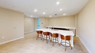 Located at 2203 N University Drive in Pembroke Pines, Florida, this club room is a well-appointed communal space designed to facilitate social gatherings and shared dining experiences. The single-level layout is efficiently organized into two distinct dining areas, connected by an open and airy floor plan that promotes easy flow and interaction throughout the space.

The dining areas feature round tables paired with modern white chairs, creating a clean and contemporary aesthetic. Natural light filters in through multiple windows, offering views of the surrounding building exterior and contributing to the room's bright, welcoming atmosphere. Neutral beige walls and light-toned tile flooring run throughout, lending the space a cohesive and polished appearance.

A standout feature of the club room is the central kitchenette bar, finished with a crisp white countertop and dark cabinetry below. Equipped with a sink and accompanied by a row of warm wood-toned bar stools, this area serves as a practical hub for food and beverage service during events. Recessed lighting overhead ensures consistent, even illumination across the entire space.

Overall, the club room presents a functional yet stylish environment, well-suited for community events, casual dining, and social gatherings in a residential setting.