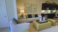 Located in the heart of Columbus, Ohio, this single-floor residence at 250 Liberty Street offers a thoughtfully designed living space that balances comfort and contemporary style. The living area serves as the centerpiece of the home, featuring a neutral color palette anchored by warm beige walls that create an inviting and relaxed ambiance. A plush white sofa adorned with teal and patterned accent pillows provides a stylish focal point, complemented by a chartreuse upholstered ottoman that doubles as a functional coffee table. A coordinating armchair and a woven area rug add layers of texture to the space. Soft, warm lighting from a table lamp enhances the cozy atmosphere, while a pair of framed abstract artworks lends a curated, gallery-like quality to the walls. The living area flows naturally into the kitchen, which features dark espresso cabinetry and a classic subway tile backsplash, creating a striking contrast to the lighter tones of the main living space. The open-concept layout promotes effortless connectivity between areas, making this residence well-suited for both everyday living and entertaining. The cohesive design throughout reflects a keen attention to detail and a commitment to functional elegance.
