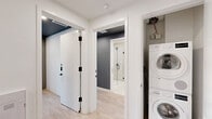Located at 1704 N 17th St in Tampa's historic Ybor City neighborhood, this modern single-story residence offers three bedrooms and four bathrooms within a thoughtfully designed floor plan. The interior showcases a clean, contemporary aesthetic defined by light hardwood flooring, crisp white walls, and bold charcoal accent walls that create visual contrast throughout.

The primary bedroom is a well-appointed retreat featuring floor-to-ceiling built-in cabinetry in a muted gray finish, an integrated workspace with a built-in desk and media center, and ample storage extending to the ceiling. A second bedroom benefits from large black-framed sliding glass doors that open to an outdoor view, allowing generous natural light to fill the room.

The galley-style kitchen is efficiently laid out with flat-front gray cabinetry, white quartz countertops, a white tile backsplash, stainless steel appliances including a range and microwave, and a single-basin sink with a matte black faucet. A dedicated laundry area with stacked washer and dryer units adds everyday convenience.

Each of the four bathrooms features large-format cream tile flooring, frameless glass-enclosed walk-in showers with floor-to-ceiling tile surrounds, and matte black fixtures and hardware throughout, lending a cohesive, upscale finish to the space.