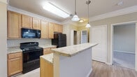 Located in Greenville, SC, this one-bedroom, one-bathroom residence offers a well-organized single-floor layout designed for comfortable everyday living. The open-concept kitchen and living area form the heart of the home, where light wood cabinetry, granite-look countertops, and black appliances — including a range, microwave, and refrigerator — define the kitchen space. A peninsula with pendant lighting overhead provides additional workspace and a natural division between the kitchen and living area. Crown molding adds a refined architectural detail throughout. The living room features light wood-tone flooring, crown molding, a ceiling fan, and a pair of French doors that invite natural light and provide outdoor access. The bedroom is generously proportioned, finished with soft carpet flooring and a ceiling fan, and connects directly to a spacious walk-in closet outfitted with extensive wire shelving and hanging rods for ample storage. The bathroom is highlighted by a large soaking tub with a tile surround and shower fixture. Neutral, warm-toned walls throughout the home create a cohesive and calming aesthetic, making this residence a practical and inviting space in Greenville, South Carolina.