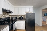 This one-bedroom, one-bathroom unit in Lowell, MA offers a well-organized single-floor layout designed for comfortable everyday living. The kitchen is a standout feature, showcasing white shaker-style cabinetry with brushed nickel hardware, dark granite-look countertops, a mosaic tile backsplash, and black appliances including a range and full-size refrigerator. Light hardwood-style flooring runs through the kitchen and dining area, where wainscoting detail adds a classic touch to the walls. The dining space comfortably accommodates a small table and chairs adjacent to the front entry. The generously sized bedroom is carpeted and bright, featuring windows that allow natural light to filter in. It offers ample room for a full bedroom suite and benefits from access to multiple closets, providing excellent storage throughout the unit. The full bathroom includes a tiled tub-shower combination with neutral stone-look tile surround. A hallway connects the main living areas, keeping the floor plan efficient and cohesive. With four closets distributed across the unit, storage is a practical strength of this home. The overall aesthetic is clean and neutral, with white walls and simple finishes that create a bright, move-in-ready environment.