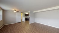 This single-floor unit offers a practical and comfortable layout designed for everyday living. The open living area is finished with warm wood-look vinyl flooring and neutral gray walls, creating a clean, modern aesthetic. A ceiling fan provides added comfort, and a wall-mounted air conditioning unit ensures climate control year-round. Baseboard heating runs throughout the unit for efficient warmth. The kitchen is seamlessly connected to the living space and is outfitted with rich dark cabinetry, light granite-style countertops, and a full suite of stainless steel appliances, including a gas range, over-the-range microwave, and refrigerator. A closet near the living area provides convenient storage. The two bedrooms are carpeted and feature neutral gray walls with natural light provided by windows fitted with blinds. The primary bedroom stands out with two built-in closets, offering generous storage capacity. The bathroom is finished with white tile surrounding a full-size soaking tub with an overhead shower, complemented by a dark-cabineted vanity with a white countertop. The overall layout is functional and well-organized, making efficient use of the available space throughout.