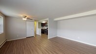 This single-floor unit offers a practical and comfortable layout designed for everyday living. The open living area is finished with warm wood-look vinyl flooring and neutral gray walls, creating a clean, modern aesthetic. A ceiling fan provides added comfort, and a wall-mounted air conditioning unit ensures climate control year-round. Baseboard heating runs throughout the unit for efficient warmth. The kitchen is seamlessly connected to the living space and is outfitted with rich dark cabinetry, light granite-style countertops, and a full suite of stainless steel appliances, including a gas range, over-the-range microwave, and refrigerator. A closet near the living area provides convenient storage. The two bedrooms are carpeted and feature neutral gray walls with natural light provided by windows fitted with blinds. The primary bedroom stands out with two built-in closets, offering generous storage capacity. The bathroom is finished with white tile surrounding a full-size soaking tub with an overhead shower, complemented by a dark-cabineted vanity with a white countertop. The overall layout is functional and well-organized, making efficient use of the available space throughout.