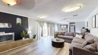 Located at 8000 Montgomery Blvd NE in Albuquerque, New Mexico, this thoughtfully designed single-floor space offers an efficient and versatile layout that maximizes every square foot. The interior is unified by light-toned hardwood-style flooring throughout, complemented by soft gray walls and crisp crown molding that lend a clean, contemporary aesthetic.

The open-plan living and dining area serves as the heart of the space. The living area features a large sectional sofa, a round dark-wood coffee table, and a striking accent wall with a sleek built-in fireplace set against a bold dark backdrop — adding depth and a focal point to the room. Flush-mount and track lighting illuminate the space effectively, while multiple sliding glass doors dressed with elegant sage green curtains flood the interior with natural light and open to a private balcony overlooking a pool.

The dining area accommodates a generous rectangular table with mixed seating and is anchored by a rustic wood sideboard beneath a large framed mirror. An adjacent kitchenette area provides added functionality with appliances including a full-size refrigerator.

A dedicated workspace area rounds out the layout, offering ample room for dual desks, office seating, and a ceiling fan — ideal for productivity. A decorative wrought-iron stair railing detail adds architectural character to this well-rounded space.